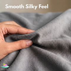 A close-up of a hand stretching and pulling a piece of smooth gray fabric to demonstrate its soft, silky texture. White text at the top reads 'Smooth Silky Feel' and a logo for 'Happy Matty' is visible in the bottom-left corner.