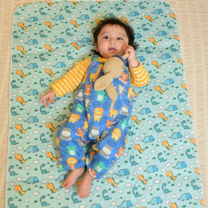 Baby lying on a Happy Matty dinosaur print bed protector mat