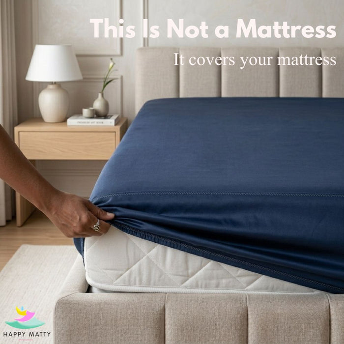 A navy blue fitted sheet is being pulled onto a mattress by a person's hand in a bedroom setting. Large text at the top reads 'This Is Not a Mattress It covers your mattress,' and the Happy Matty logo appears in the bottom left corner.