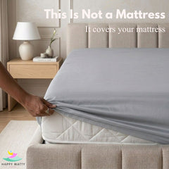 A hand pulls a light gray fitted sheet over a white mattress in a styled bedroom setting. Large text at the top reads, 'This Is Not a Mattress.